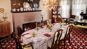 A dining room with a brick fireplace, a chandelier, and a table set for six with floral centerpieces. - Luther Ogden Inn (Cape May)