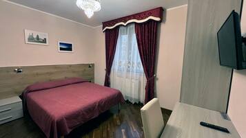 Ein Hotelzimmer mit einem Bett, einem Schreibtisch, einem Fernseher, einer Kristallleuchtre und einem Fenster mit Vorhängen.