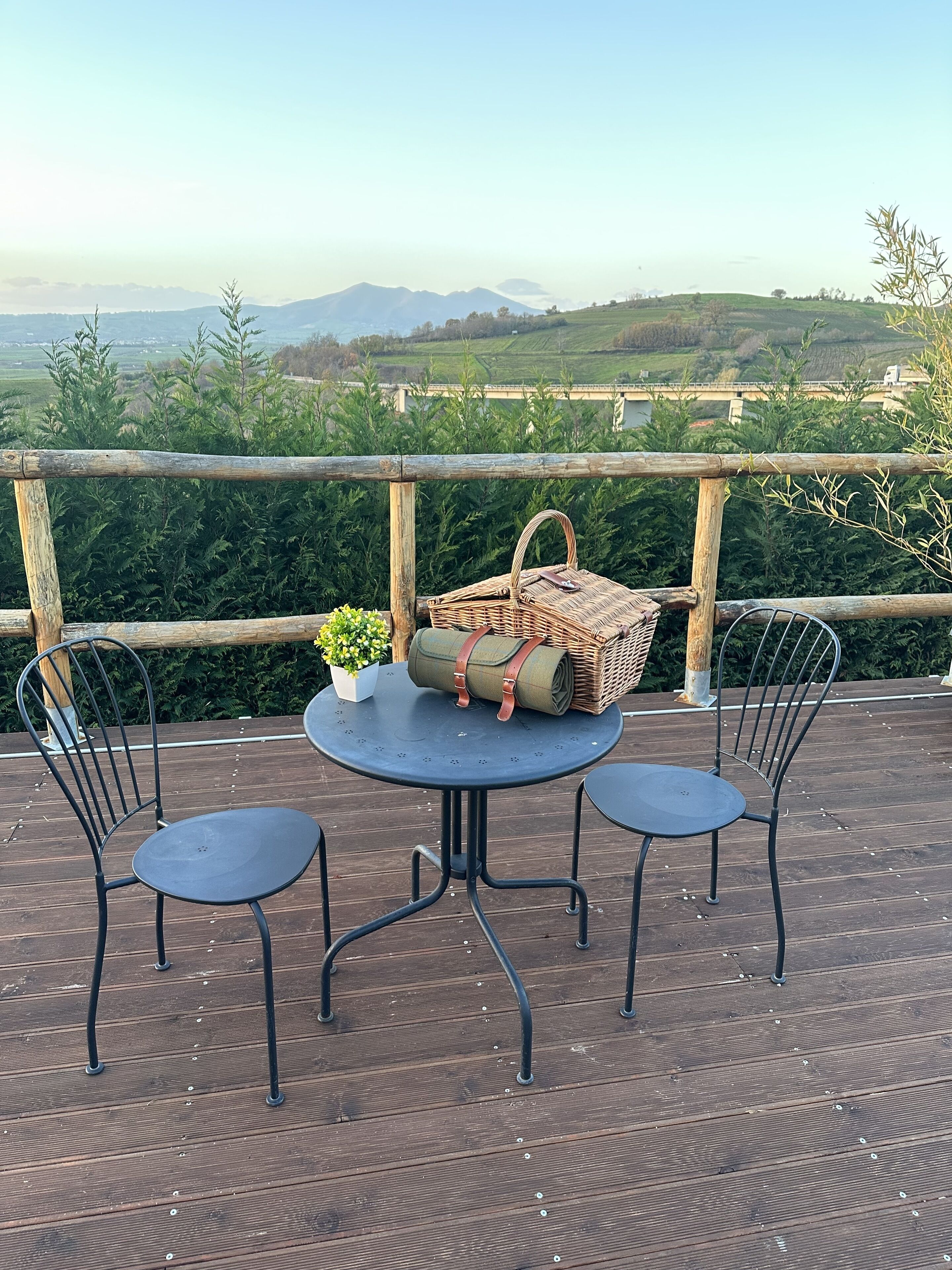 Une terrasse en bois avec deux chaises en métal et une petite table ronde, un panier en osier et une plante en pot.