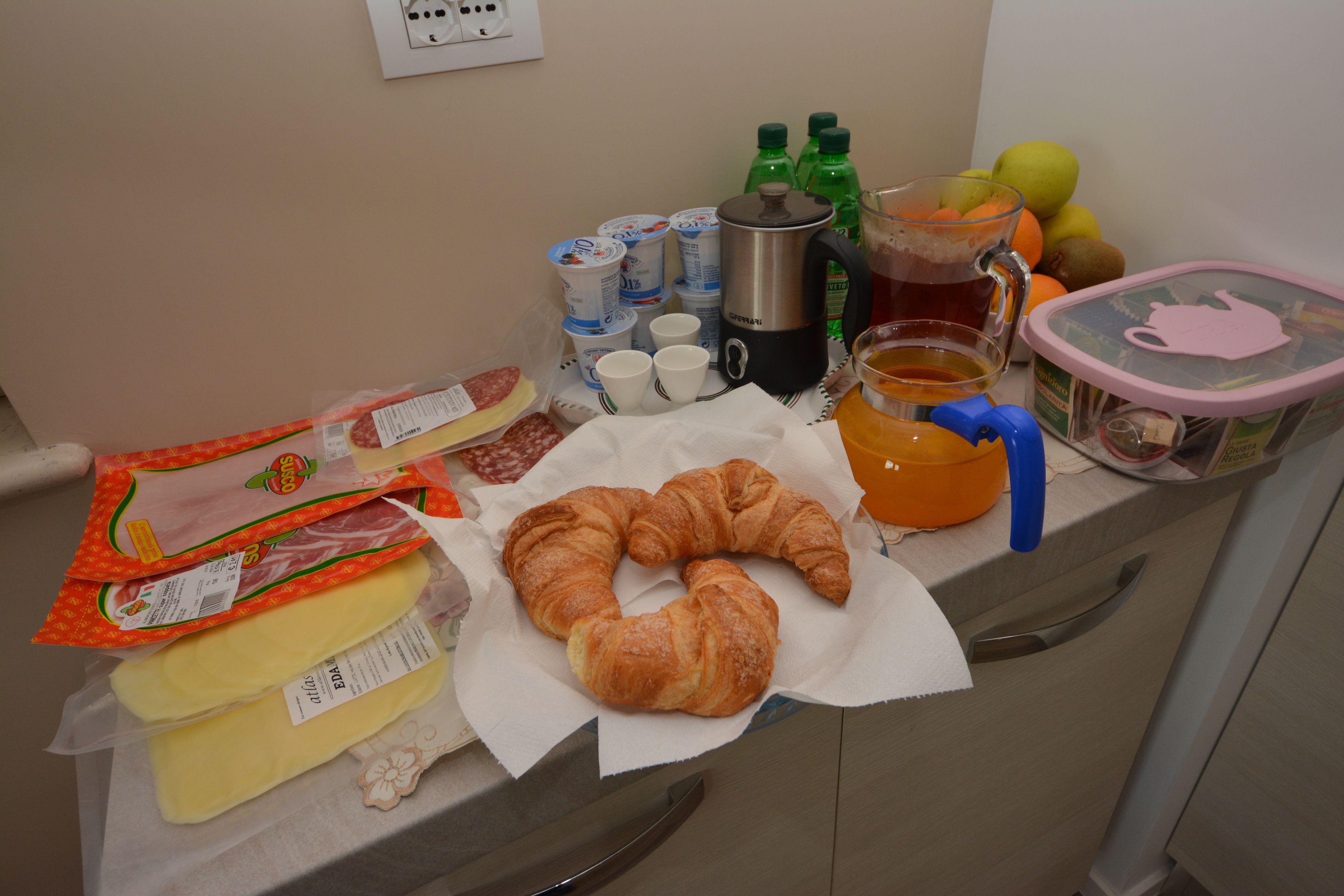 A breakfast table with croissants, coffee, tea, fruit, and packaged food.
