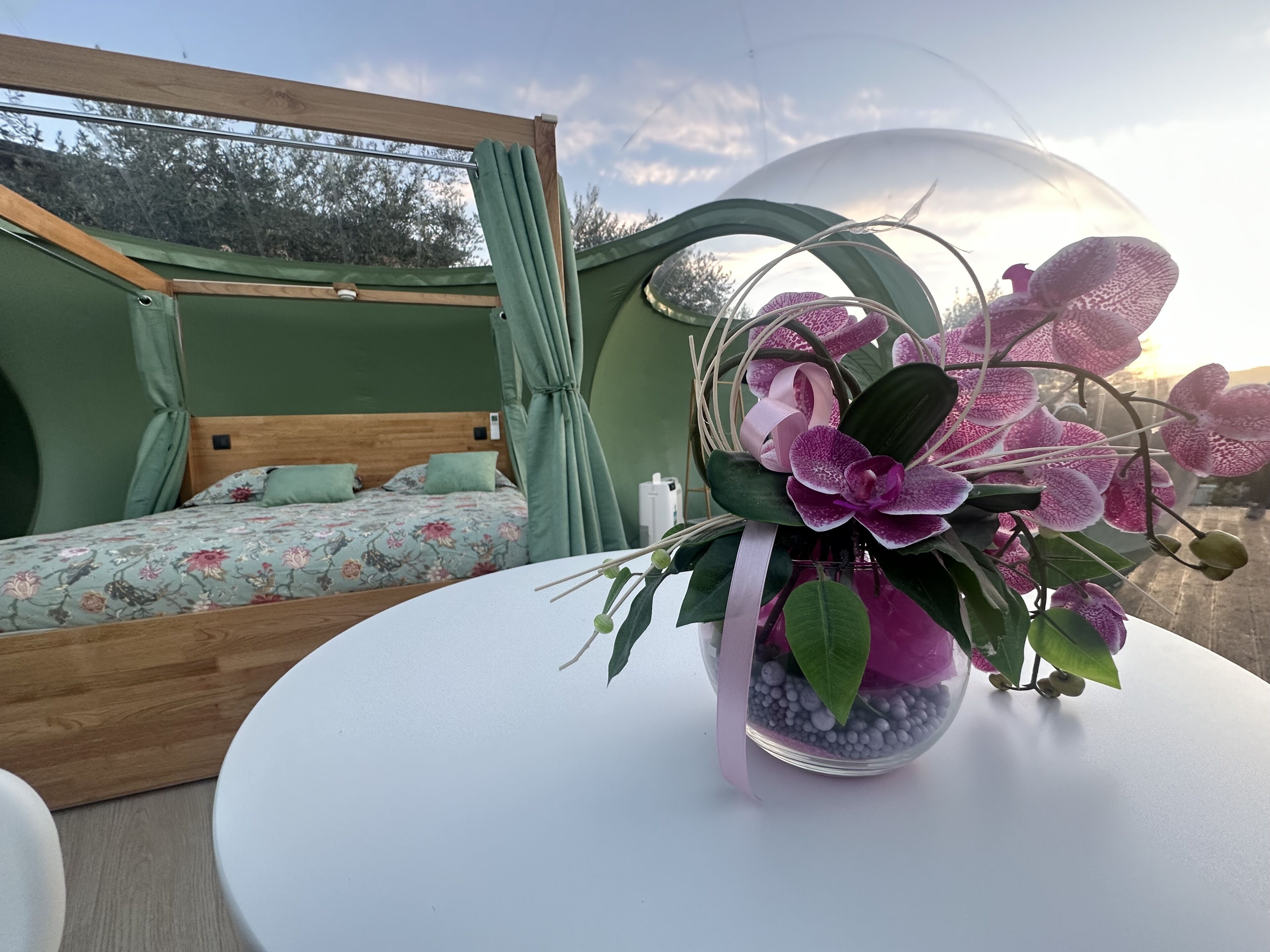 Een slaapkamer met een bed, een raam en een tafel met bloemen.