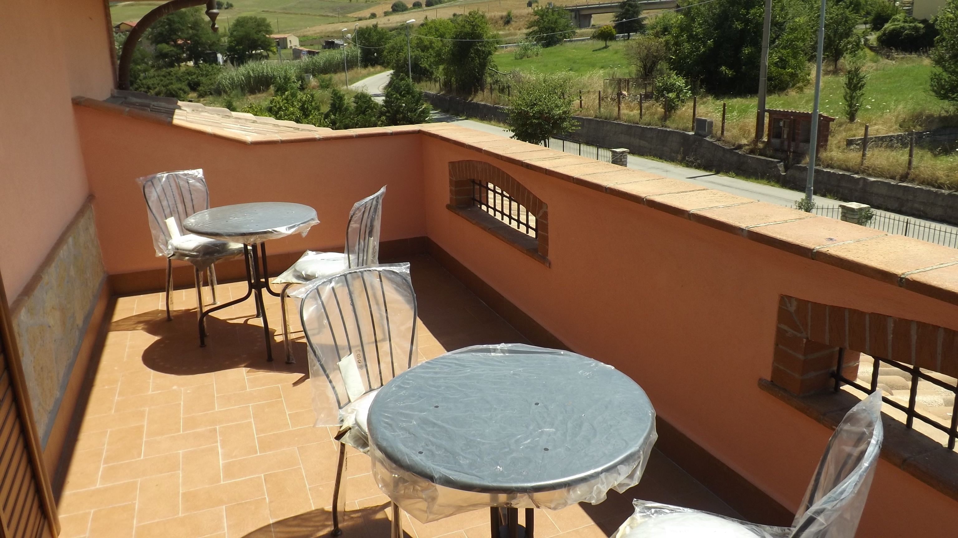Un balcon avec une table et des chaises, une vue sur un paysage rural et un mur en pierre.