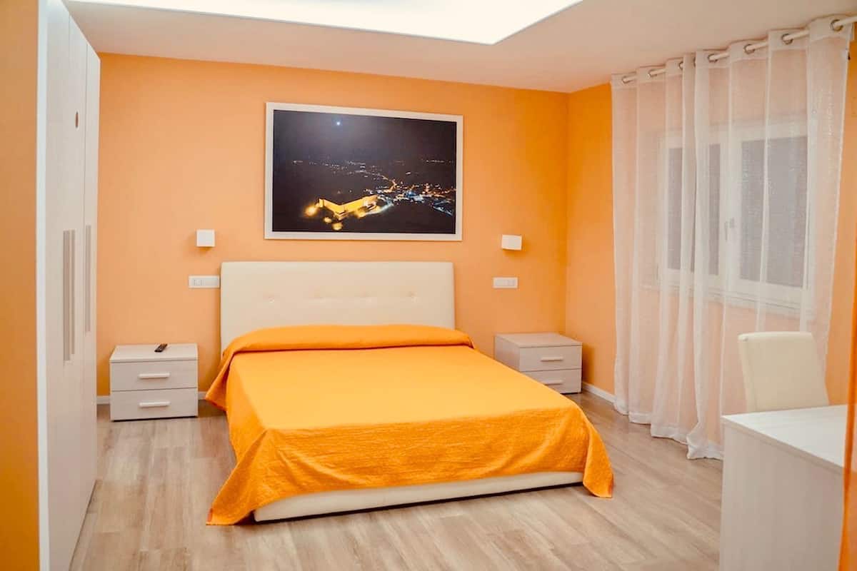 A bedroom with a bed, nightstands, a desk, and a window with curtains.