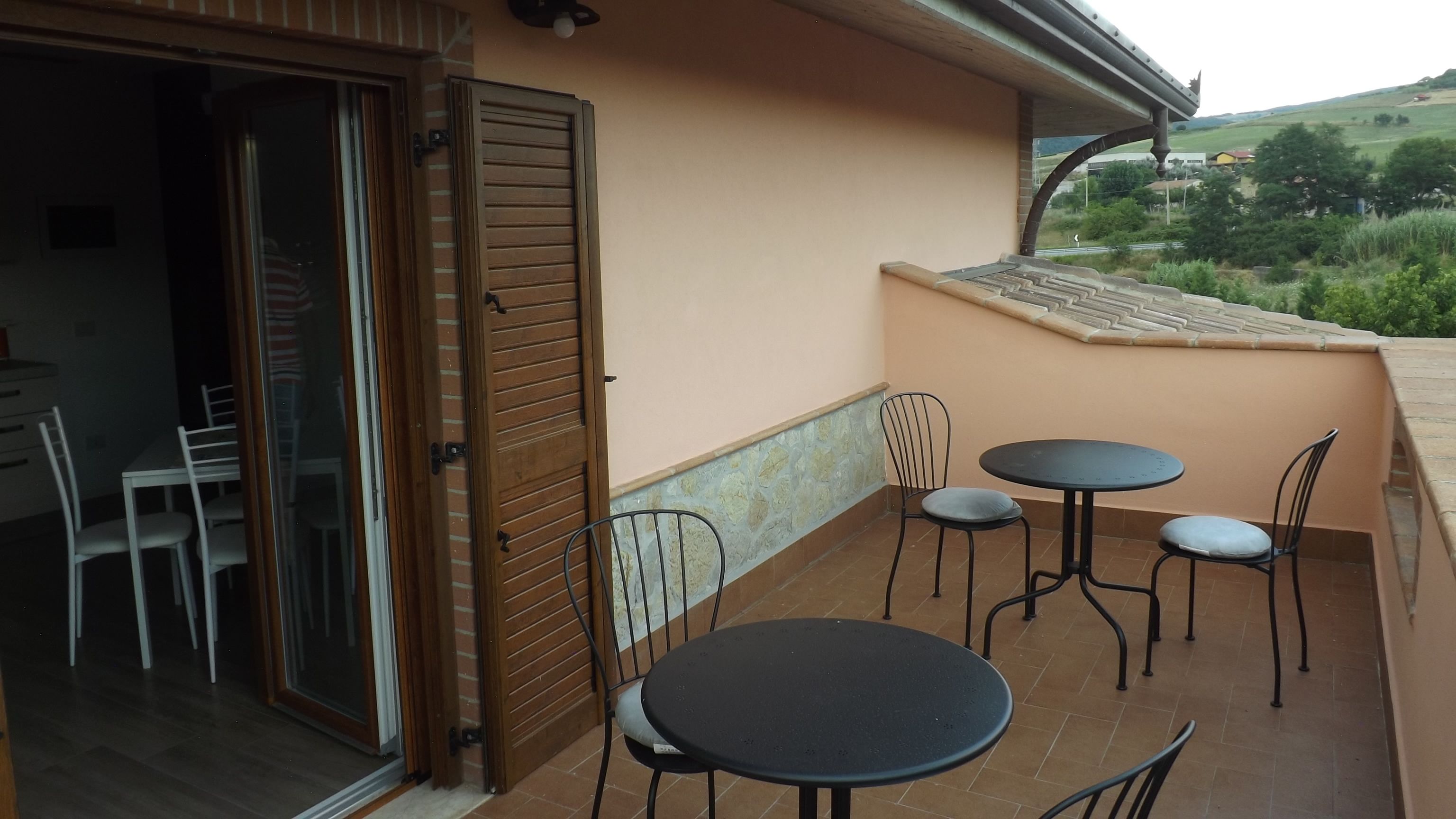 A balcony with a table and chairs, a sliding glass door, and a view of the countryside.