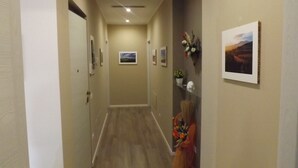 Un pasillo con cuadros enmarcados en las paredes, piso de madera y una puerta al final.