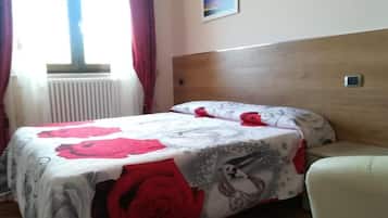 A bedroom with a bed, a wooden headboard, a window with curtains, a radiator, and a small painting on the wall.