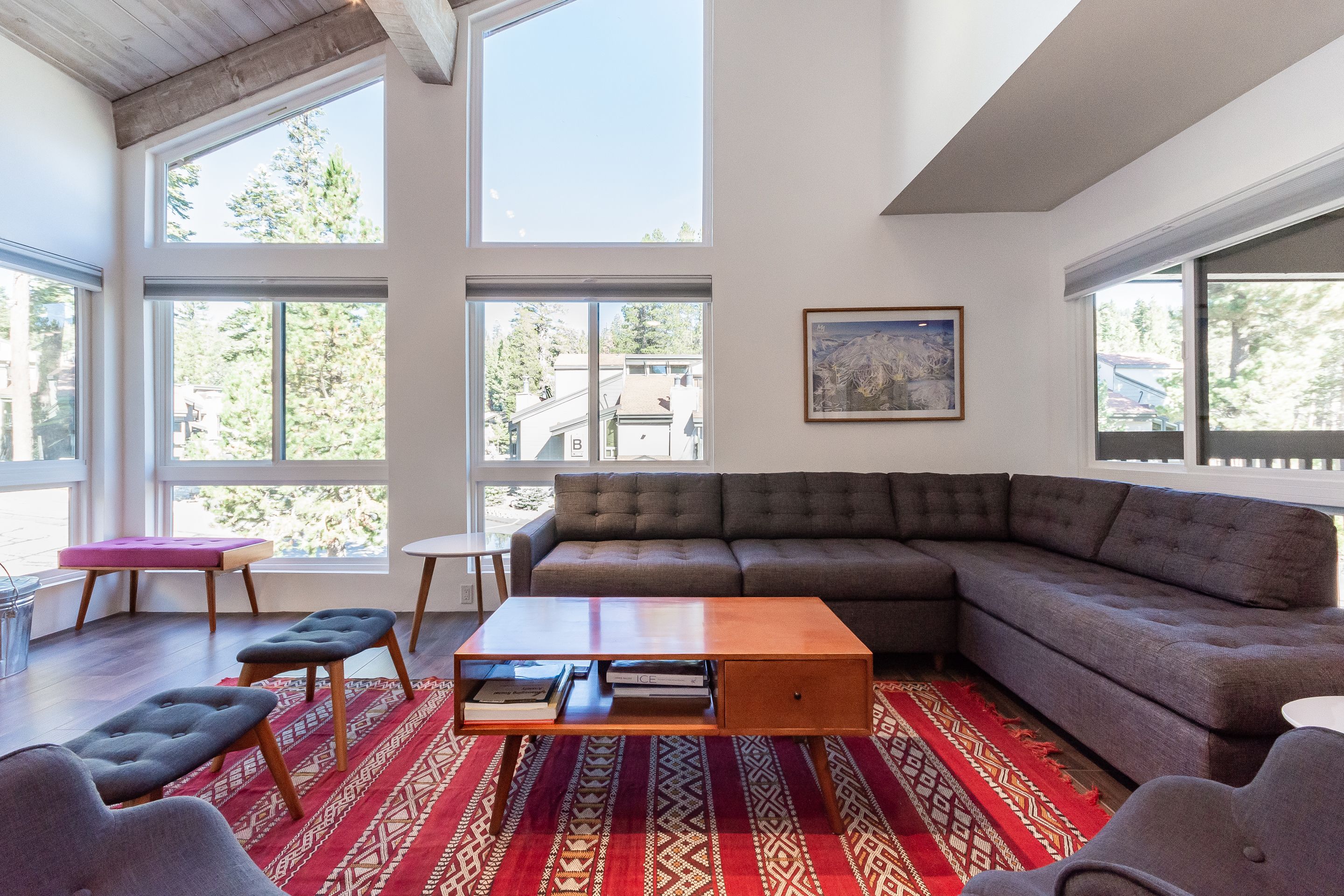Un salon moderne doté de grandes fenêtres, d’un canapé d’angle, d’une table basse et d’un tapis à motifs.