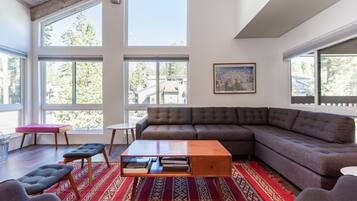 A modern living room with large windows, a sectional sofa, a coffee table, and a patterned rug.