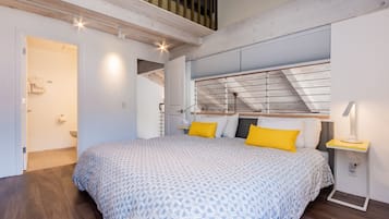 A bedroom with a large bed, wooden flooring, a skylight, and a small bedside table with a lamp.