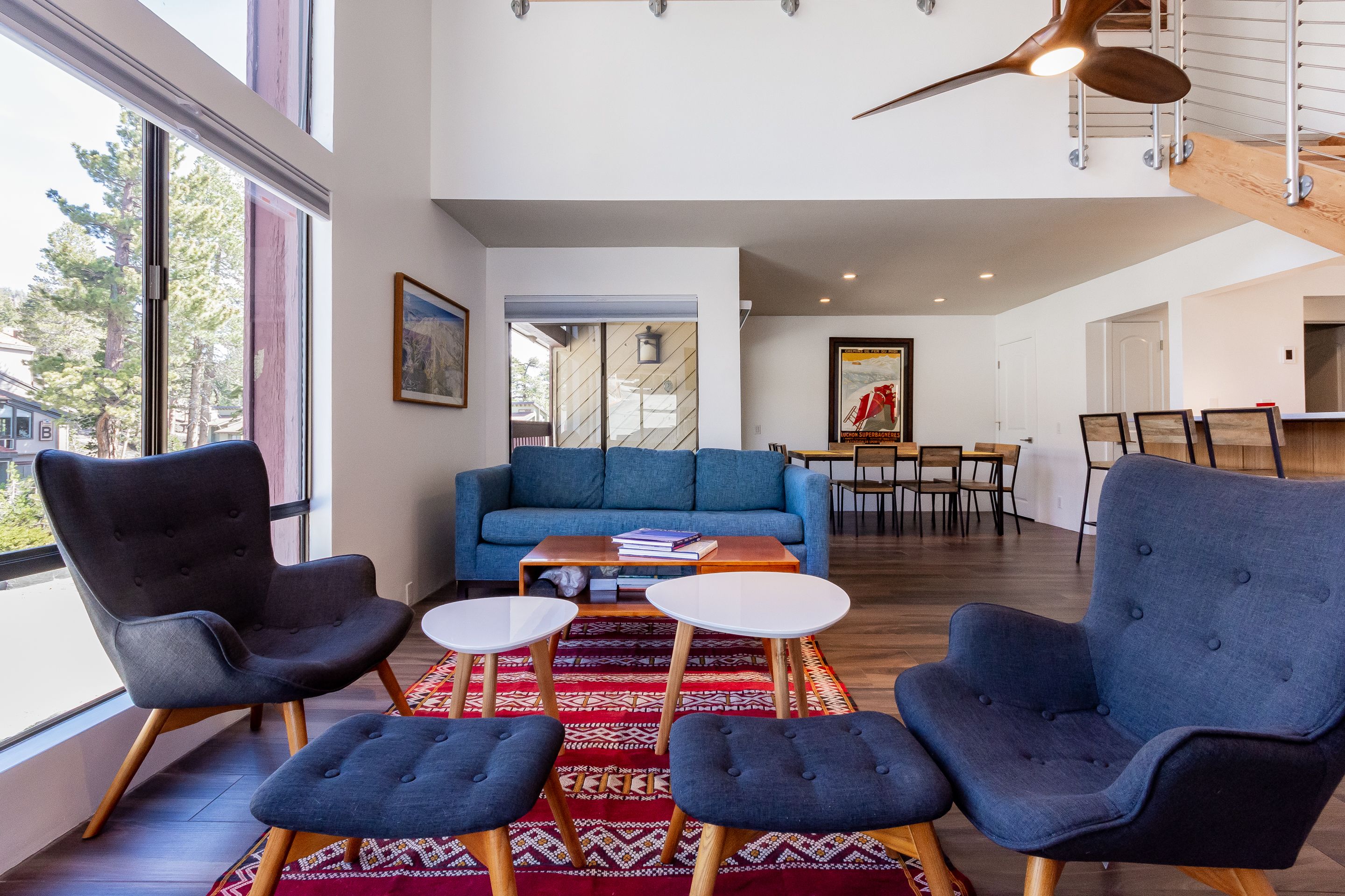 A modern living room with a blue sofa, two armchairs, a coffee table, and a dining area in the background.