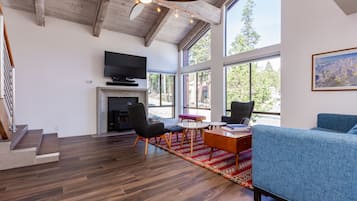 A spacious living room with a fireplace, a television, and a large window offering a view of the outdoors.