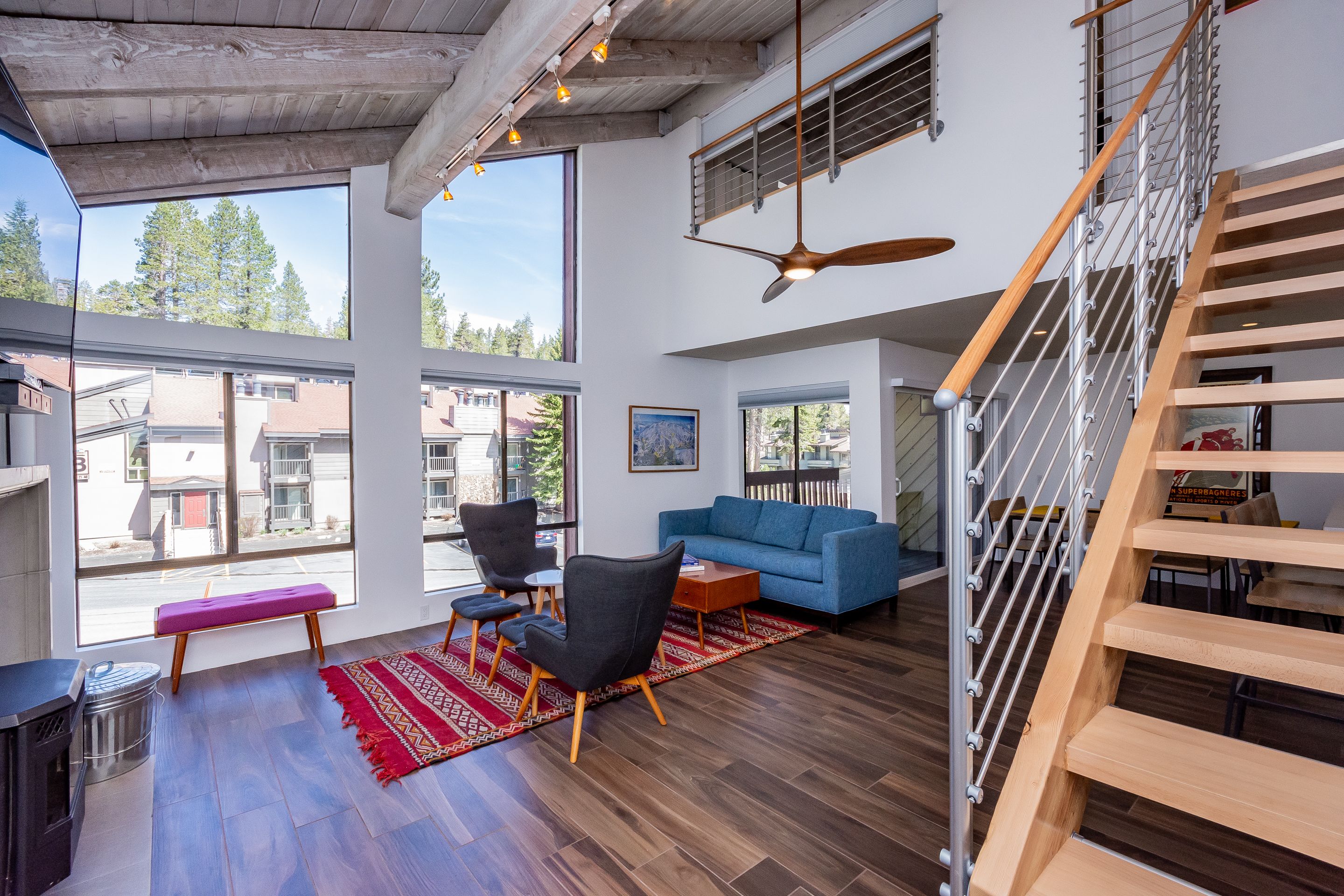 A spacious living area with a blue sofa, wooden flooring, and a large window offering a view of the outside.