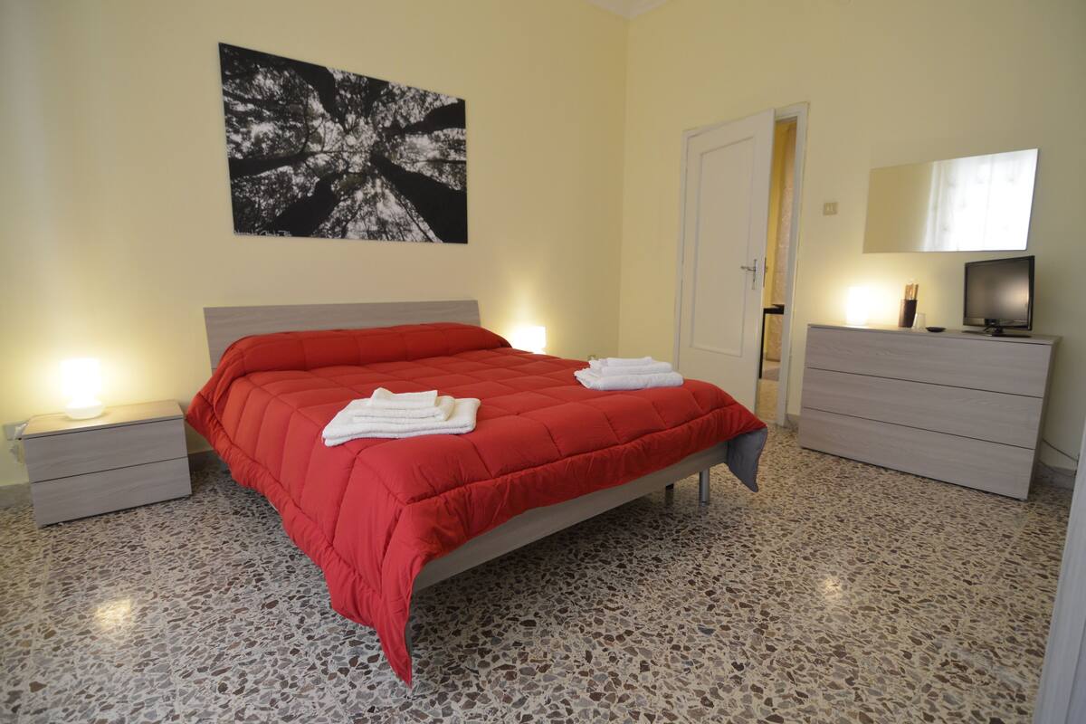 Ein Schlafzimmer mit Bett, Nachttischen, Kommode, Fernseher und einem Bild an der Wand.