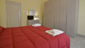 A bedroom with a red bedspread, a television, a lamp, and a wardrobe. - Efesto Bed & Breakfast (Catania)