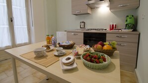 A kitchen with a dining table set with food and drinks, a coffee maker, and cabinets. - Efesto Bed & Breakfast (Catania)