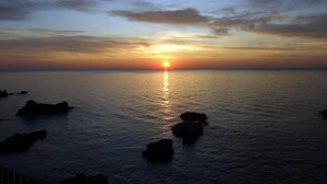 A sunset over a calm sea with rocks in the foreground. - Efesto Bed & Breakfast (Catania)