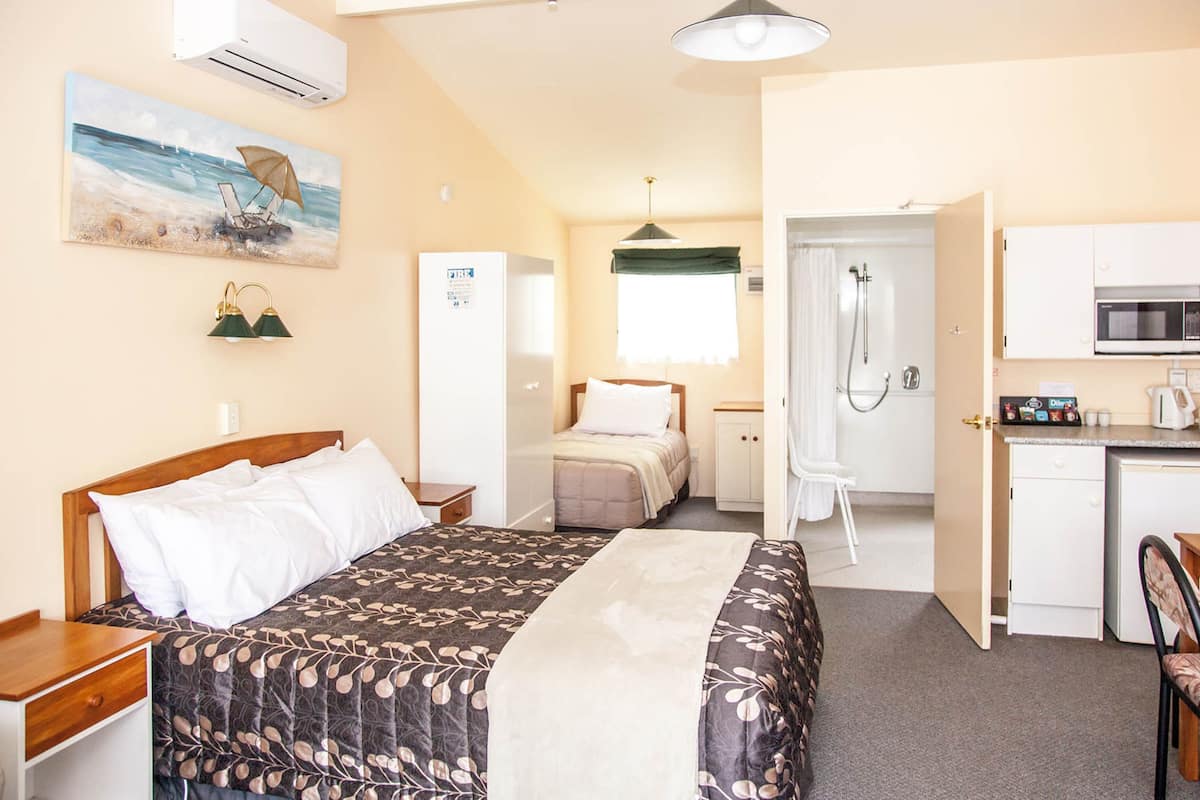 A hotel room with a bed, a desk, a kitchenette, and a bathroom.