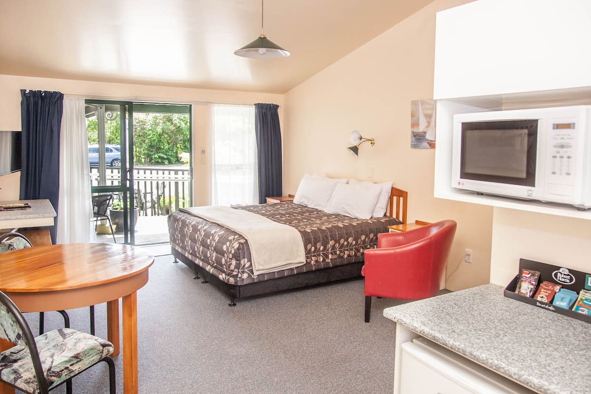 A hotel room with a bed, a desk, a chair, a microwave, and a small kitchenette.