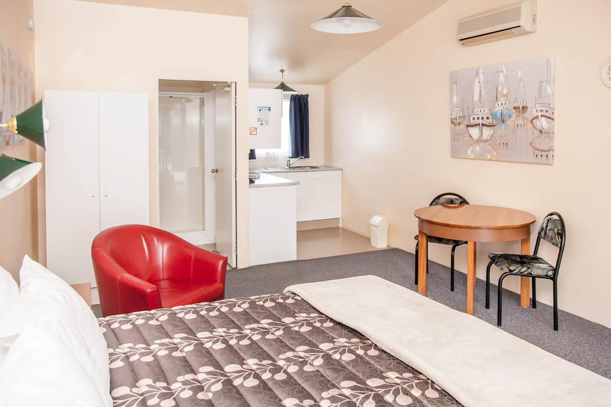 A bedroom with a bed, a red chair, a wooden table, a small desk, and a painting on the wall.