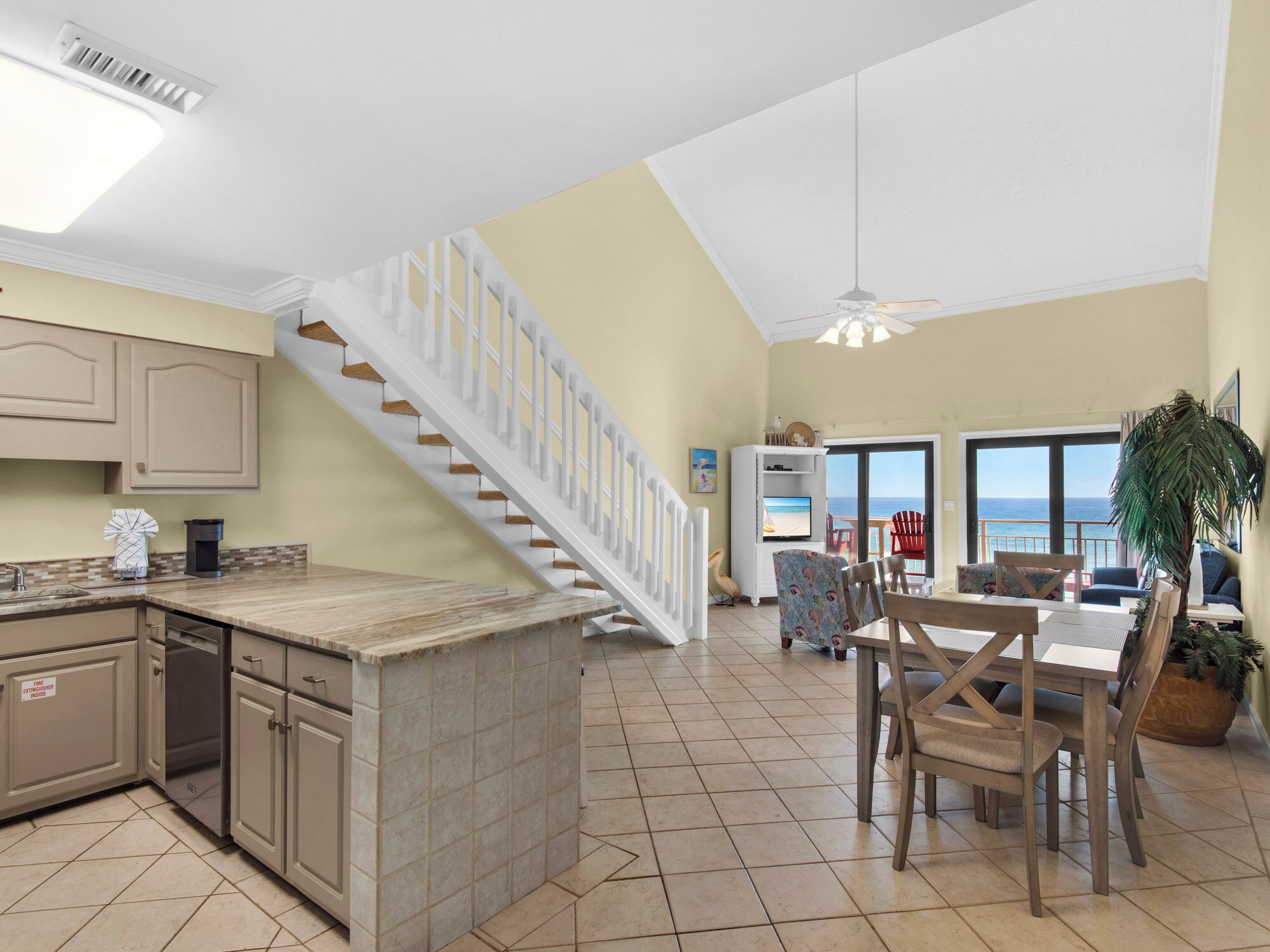 A spacious kitchen with a central island, a dining area with a view, and a staircase leading to a balcony with a view of the ocean.