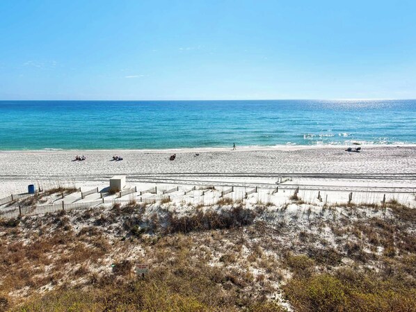 A beach with a clear sky, sandy shore, and a few people walking.