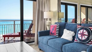 Een balkon met uitzicht op de oceaan, een blauwe bank met marinekussens en een rode stoel.