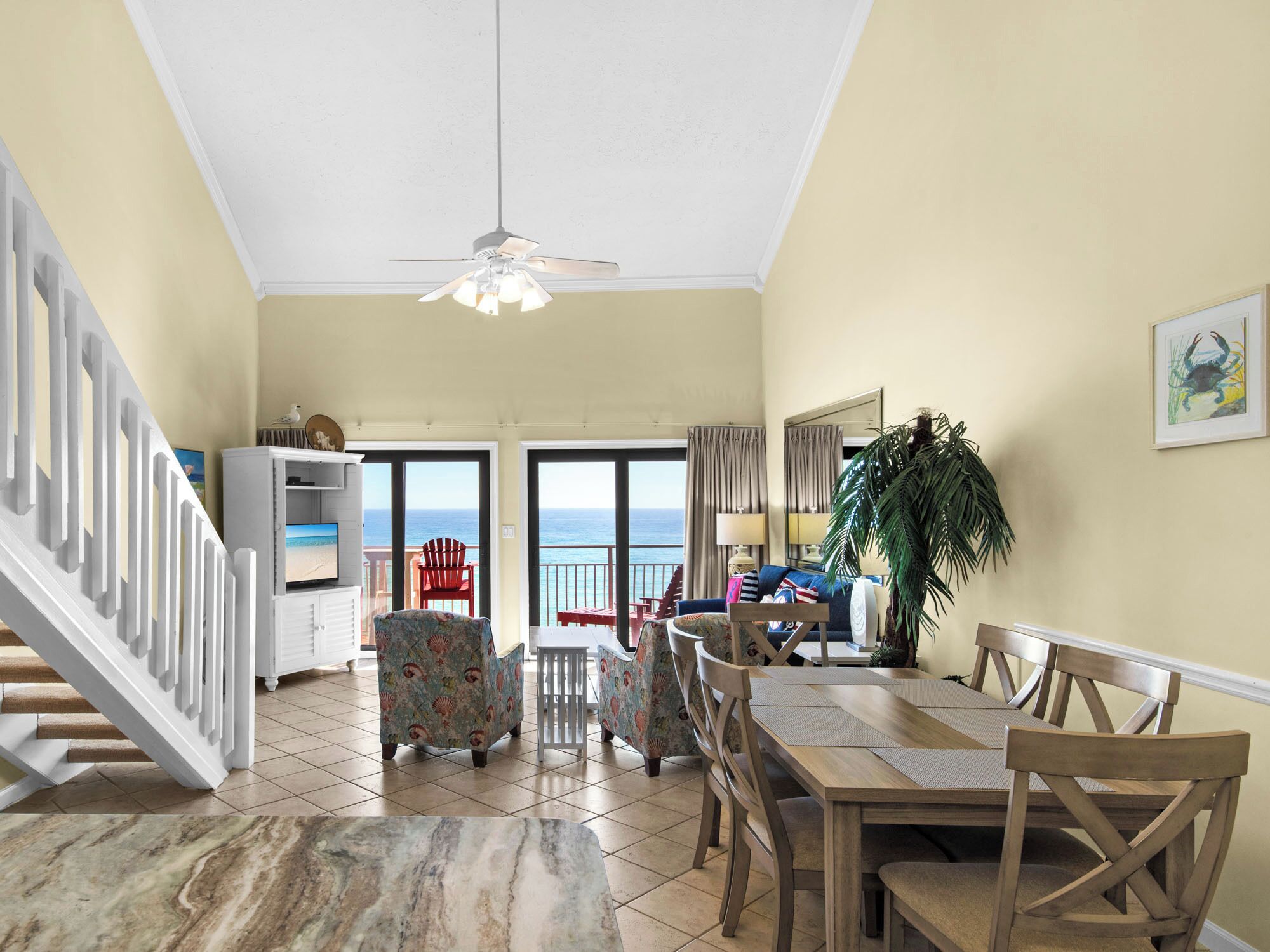 A spacious living area with a dining table, chairs, a television, and a view of the ocean.