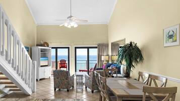 A spacious living area with a dining table, chairs, a television, and a view of the ocean.
