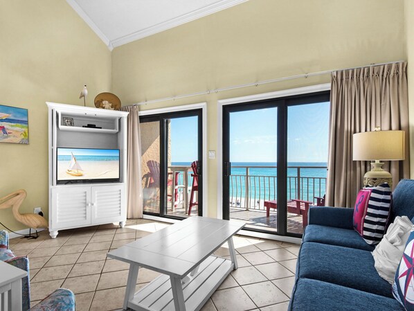 Una sala de estar con televisor, sofá y una mesa. Hay un balcón con vistas a la playa y al océano.