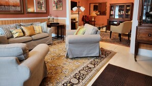 Un salon comprenant un canapé, un fauteuil et un pouf, un tapis à motifs et un meuble en bois.