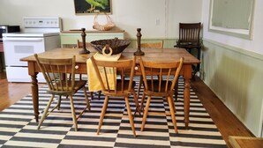 Un coin repas avec une table en bois, quatre chaises, un tapis à motifs, une lampe de style vintage, un panier en osier et une affiche accrochée au mur.