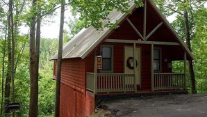 Eine kleine, rote Holzhütte mit Veranda, umgeben von Bäumen.