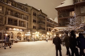 A snow-covered square with buildings, balconies, and a few people walking.