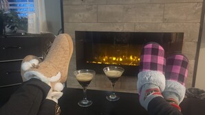 Una habitación acogedora con chimenea, dos vasos de una bebida oscura y un par de pantuflas.