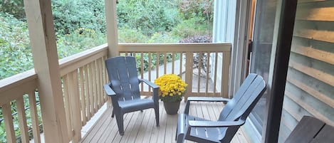 Een overdekte veranda met houten vloer, een leuning en twee stoelen.