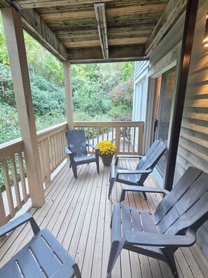 A covered porch with wooden flooring, a railing, and two chairs.