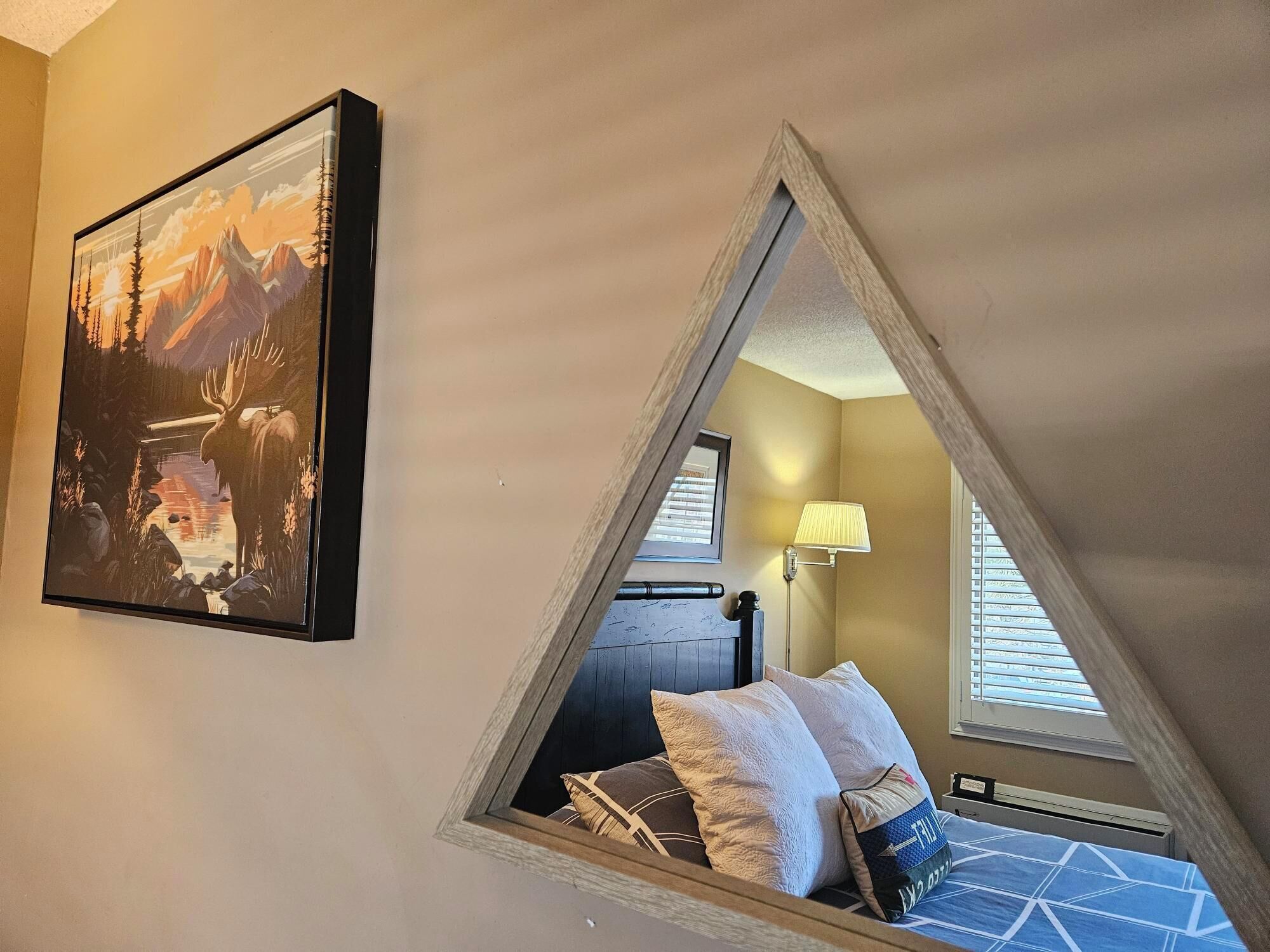 Una camera da letto mansardata triangolare con un letto, cuscini, una lampada e un quadro appeso al muro.