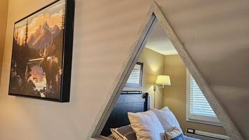 Una camera da letto mansardata triangolare con un letto, cuscini, una lampada e un quadro appeso al muro.