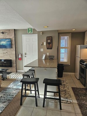 A modern kitchen with a central island, bar stools, a built-in oven, and a refrigerator.