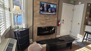 Una sala de estar con televisión montada en una pared de madera, chimenea, sofá y una mesita.