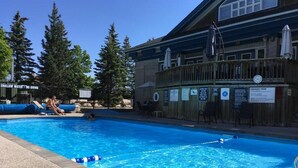 Una piscina con plataforma de madera, rodeada de árboles y un edificio con terraza.
