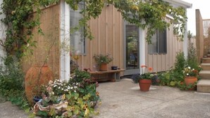A wooden house with a covered porch, potted plants, and a bench. - Mapua Studio  High Quality Accommodation  (Mapua (Ruby Bay))