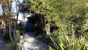 A garden with gravel paths, various plants, and a blue shed. - Mapua Studio  High Quality Accommodation  (Mapua (Ruby Bay))