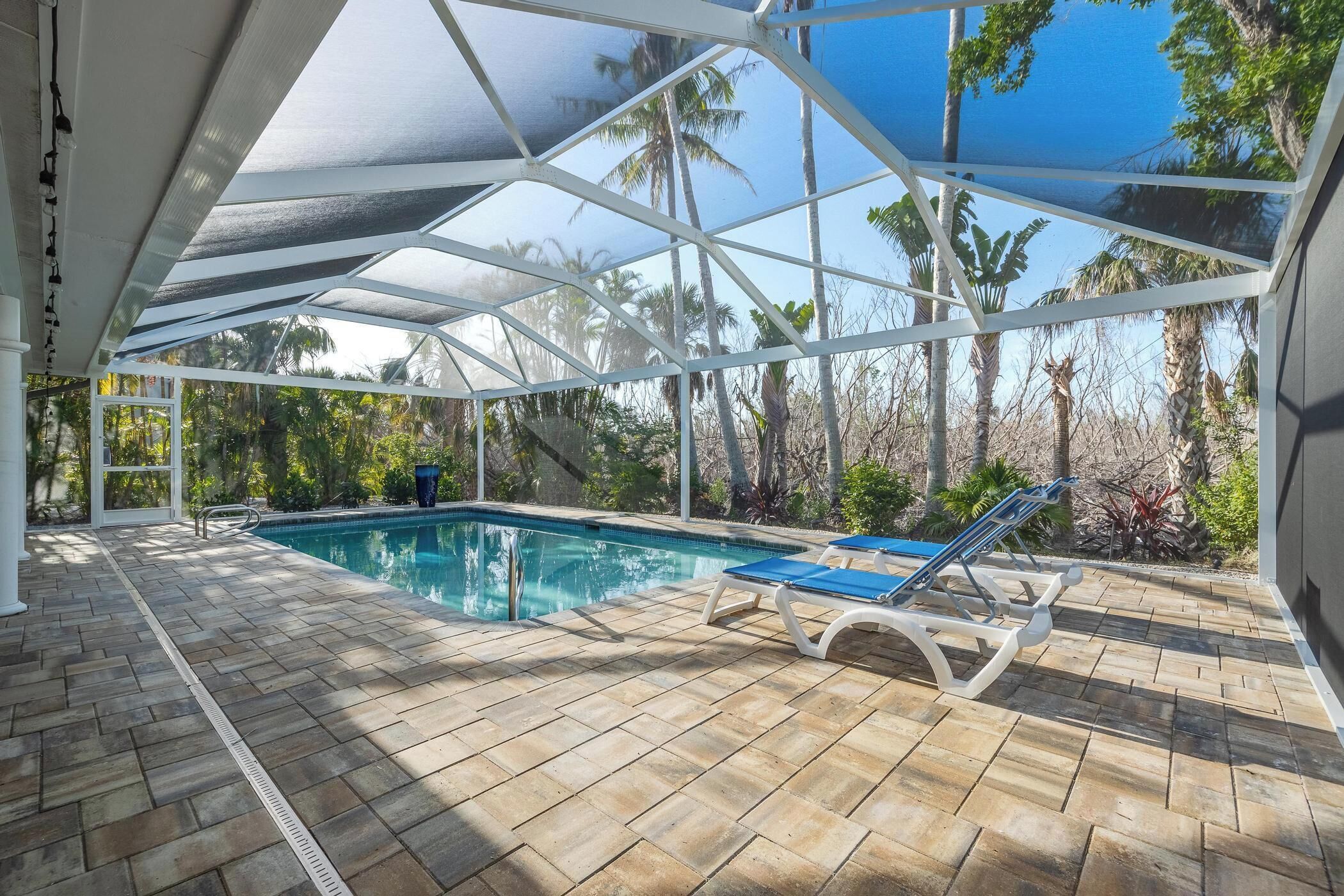A covered outdoor swimming pool with lounge chairs, surrounded by tropical vegetation.