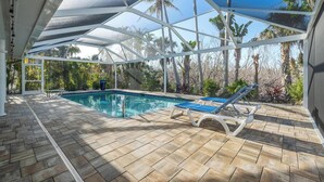 Una piscina scoperta coperta con lettini, circondata da vegetazione tropicale.