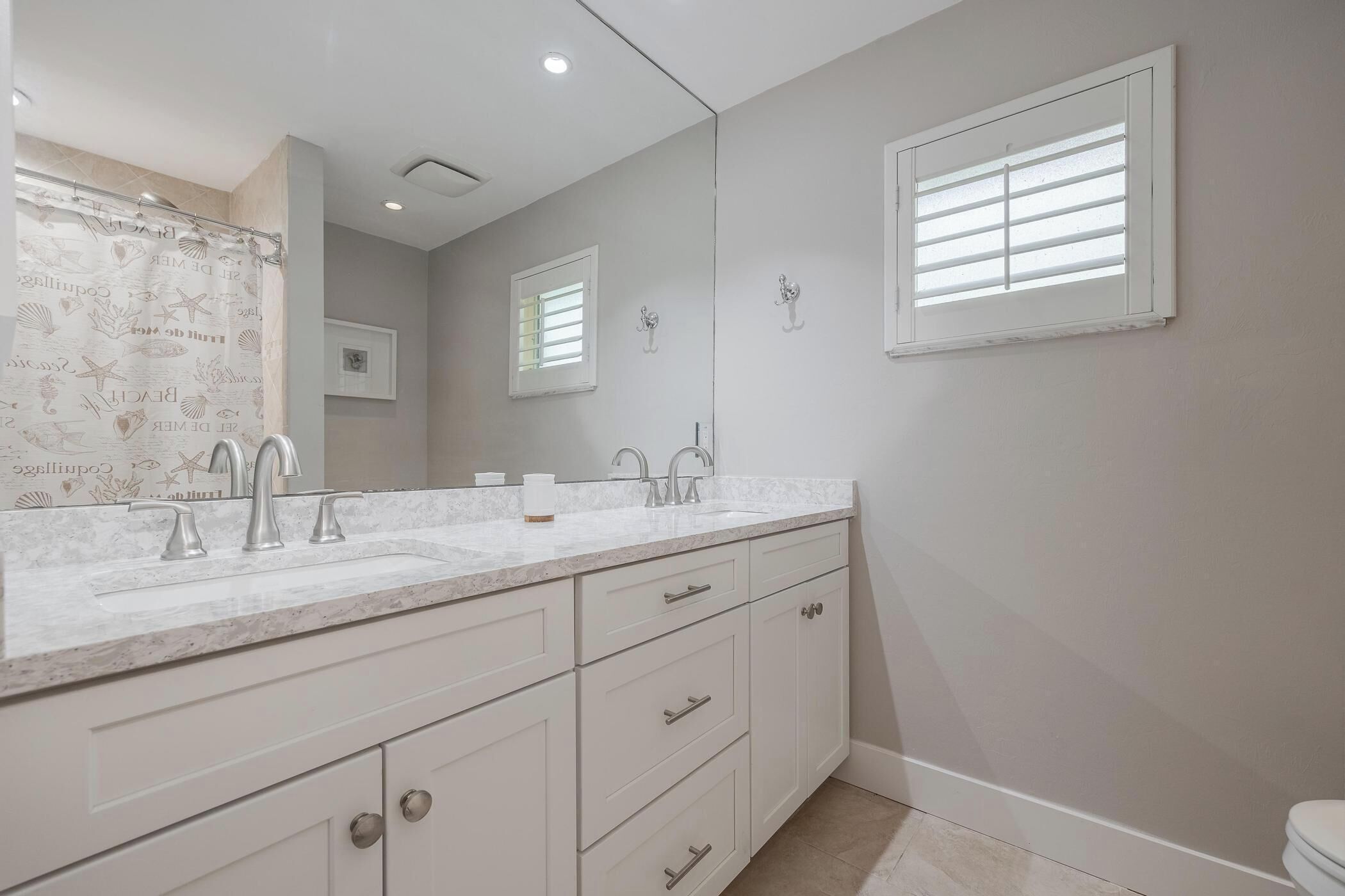 A bathroom with a double sink, white cabinets, and a shower curtain with a sea theme.