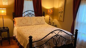A bedroom with a bed, a nightstand, a lamp, a ceiling fan, and a window with curtains.