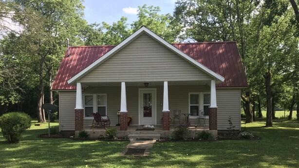 A single-story house with a gabled roof, a front porch with white columns, and a brick foundation.