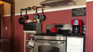 A kitchen with a stainless steel stove, a microwave, and a coffee maker. There is a red teapot on the stove, and a sign on the wall that says "I like my cream & sugar with a touch of coffee."