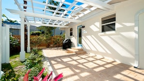 A covered patio area with a pergola, a barbecue grill, and a pathway leading to a door. - Anna Cabana B: Pool Home, AMI North End, 2 Blocks to Beach by Anna Maria Life Vacation Rentals (Anna Maria)